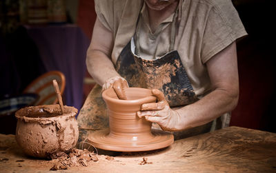 Midsection of man making pot on wheel
