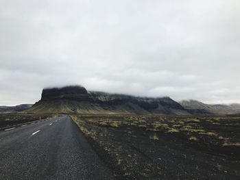 Country road leading towards mountains against sky