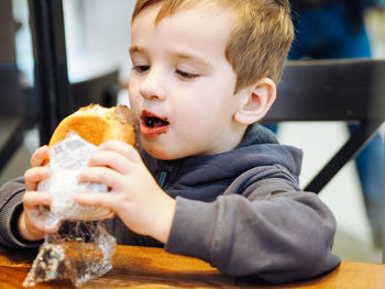 Toddler boy in casual clothes eating a chocolate bun in a food court there is chocolate on his face