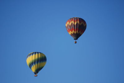 Low angle view of hot air balloons flying in clear blue sky