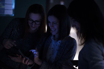 Cheerful friends using smart phone in darkroom