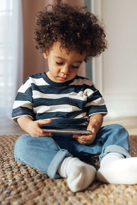 Cute boy holding mobile phone while sitting on floor