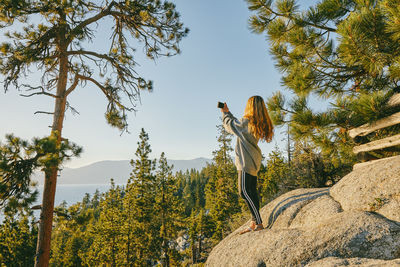 Young woman taking a picture of sunset over lake tahoe.