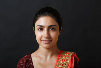 Portrait of young woman standing against black background