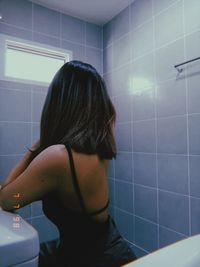 Rear view of woman standing in bathroom