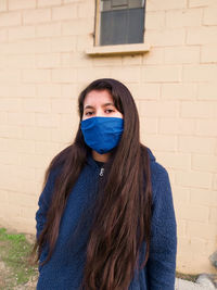 Portrait of young woman wearing mask standing against wall