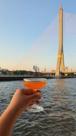 A hand is holding a glass of cocktail with beautiful view of bangkok and chaophraya river. 
