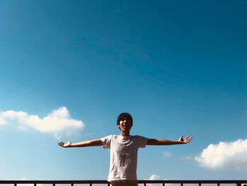 Young man with arms outstretched standing against sky