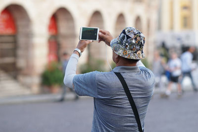 Rear view of man photographing with smart phone while standing on street