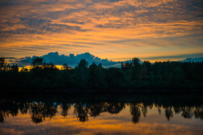 Reflection of silhouette trees in lake against sky during sunset