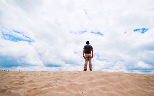 Rear view of man standing on beach against sky