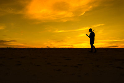 Silhouette man standing on field against orange sky