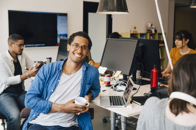 Portrait of male computer programmer sitting by colleagues at desk in office