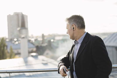 Businessman listening music and looking buildings while standing at office