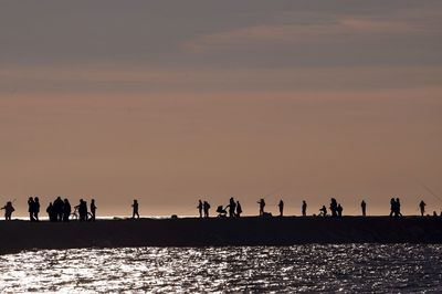 Silhouette people standing by sea against sky during sunset