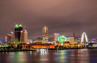 Illuminated buildings by river against sky at night