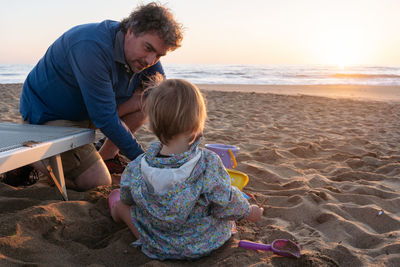 Father and child sitting at the beach in the sunset