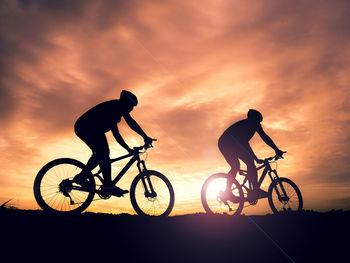 Silhouette people riding bicycle against sky during sunset