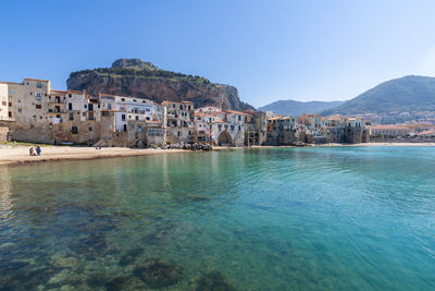 Buildings by sea against clear blue sky