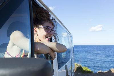 Portrait of smiling young woman by sea against sky