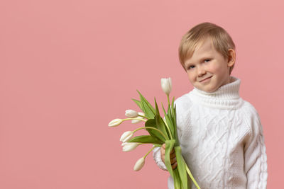 Portrait of smiling girl holding red flower against gray background