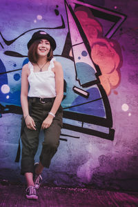 Portrait of smiling young woman standing against wall