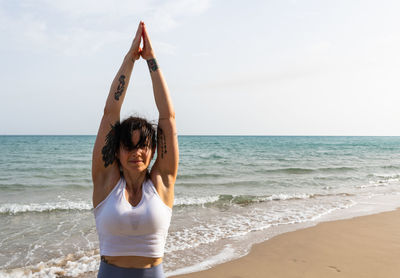 Smiling woman exercising at beach against sky