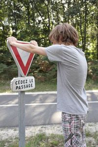 Side view of boy touching sign by road