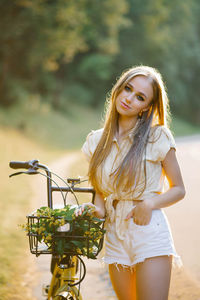 Young beautiful woman standing next to a bicycle with a wicker basket full of flowers in the forest