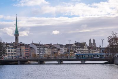 View of buildings by river against cloudy sky