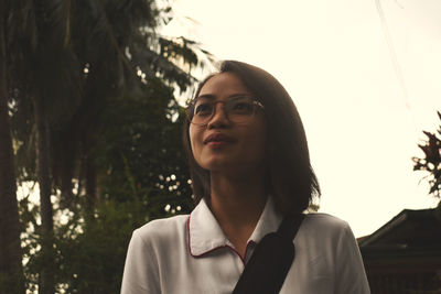 Portrait of beautiful young woman looking away against trees