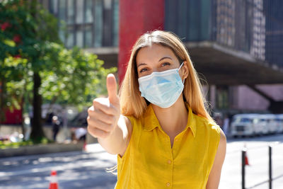 Optimistic young woman wearing protective surgical mask showing thumbs up in sao paulo city, brazil
