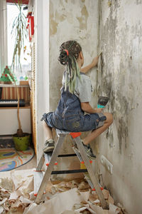 Girl repairing room and unhanging wallpaper. maintenance and repair, family lifestyle, indoor