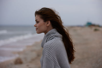 Side view of young woman looking away against sky