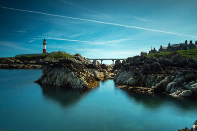 Panoramic view of lighthouse by rock formations in sea against sky