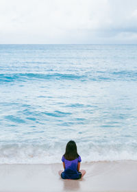 Rear view of woman sitting at beach against sky