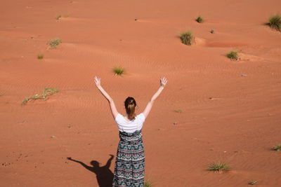 Rear view of woman standing with arms raised in desert on sunny day