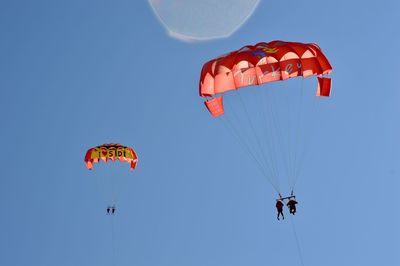 Low angle view of people paragliding against clear sky