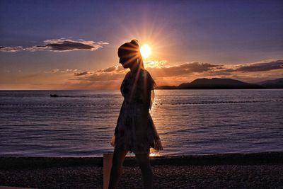 Woman standing at beach against sky during sunset