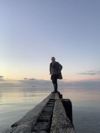 Man standing on pier over sea against sky during sunset