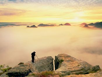 Man standing on rock against sky during sunset