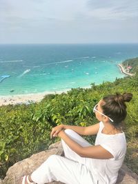 Rear view of woman sitting on beach against sky