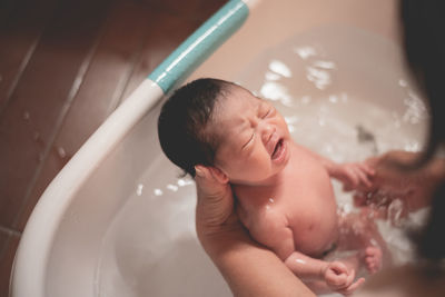 Cropped hands of mother bathing cute daughter in bath tub at home