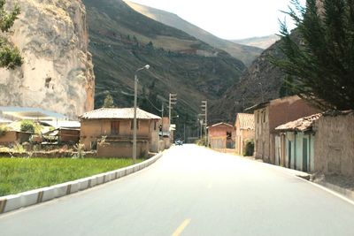 Road amidst buildings and mountains against sky