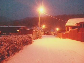 Illuminated road amidst snow against sky at night