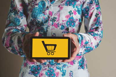 Midsection of woman holding smart phone with shopping cart icon