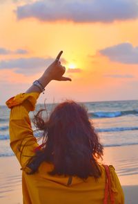 Rear view of woman gesturing shaka sign at beach during sunset