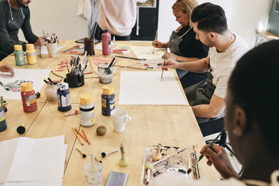 Male and female students practicing painting while sitting at table in art class