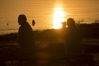 Rear view of silhouette woman sitting on beach during sunset