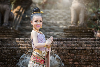 Portrait of smiling girl with hands clasped against temple